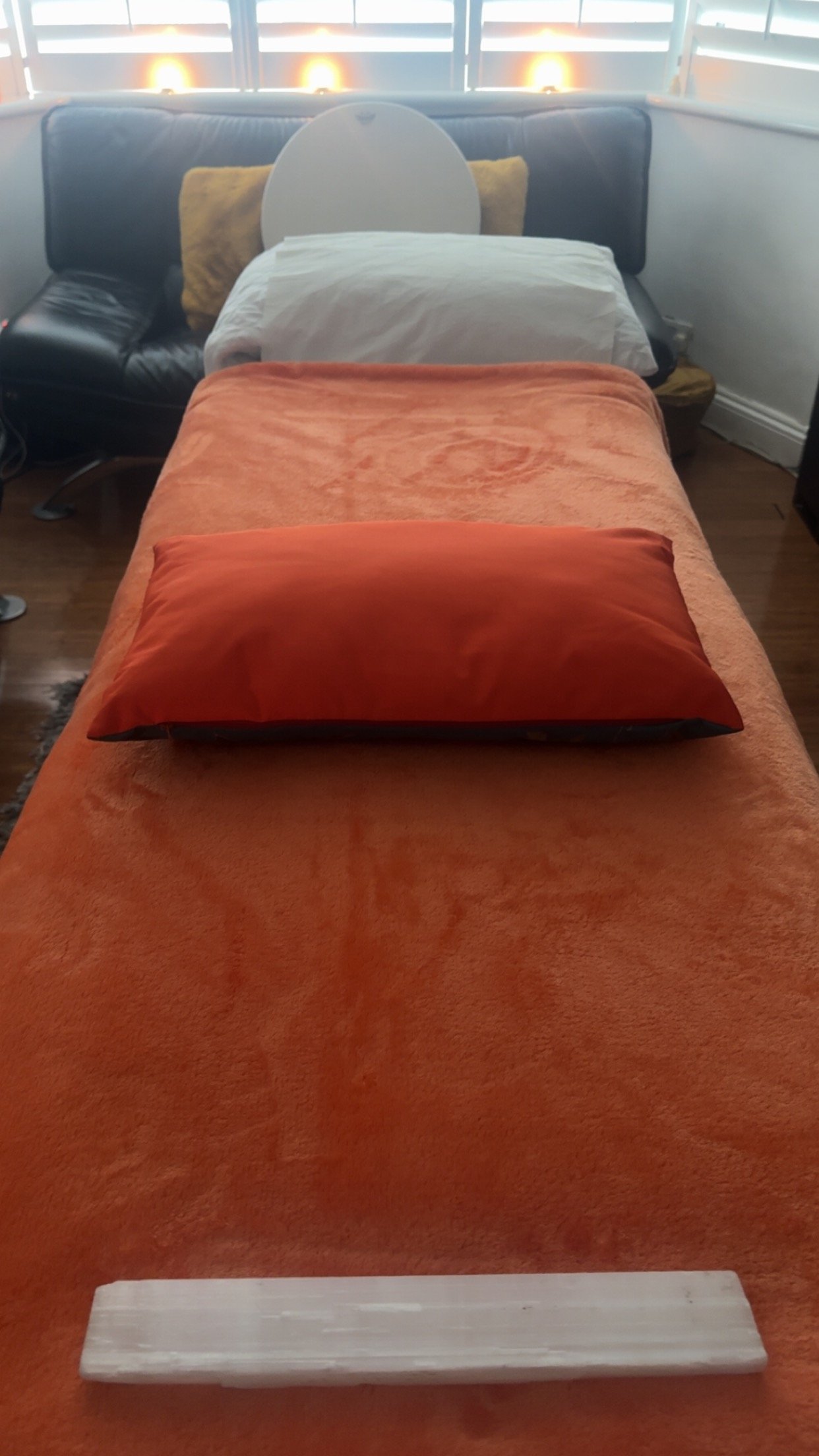 Picture of a Therapy Couch/bed set up with orange blanket and pillow with Candles in the background